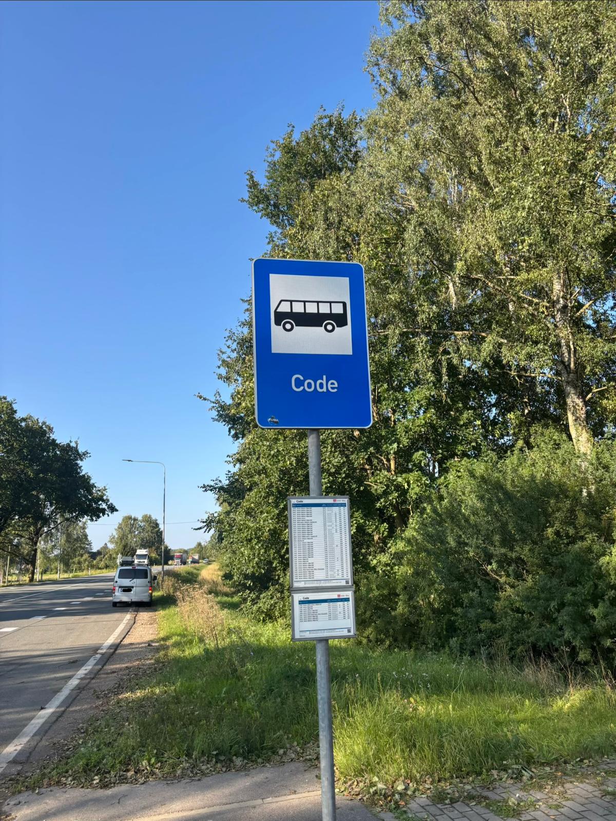 A blue bus stop sign marked Code beside a road, with a van parked farther down