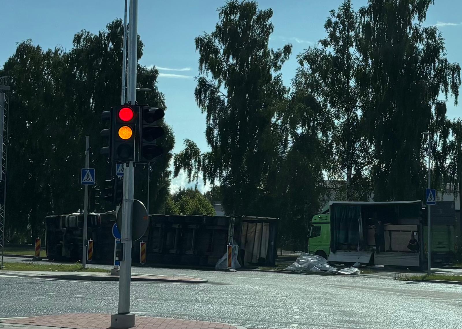 An overturned truck near an intersection, with traffic lights and another truck nearby